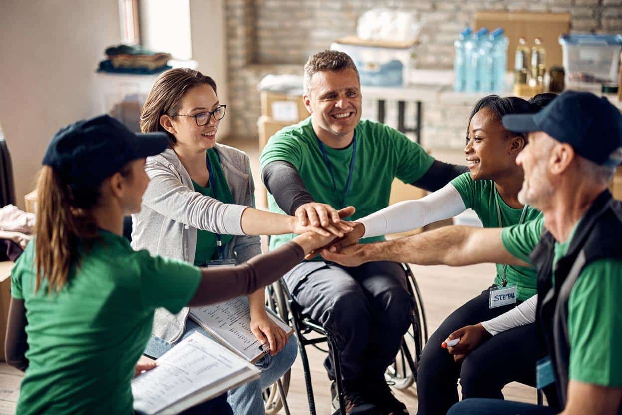 A group of people acting in a supportive manner, they all have their arms outstretched to meet in the middle with their hands on top of each other.